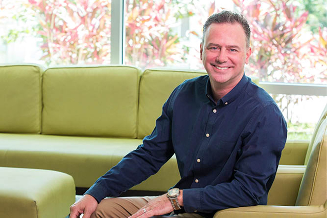 A man named Jamie Deruyter Leaning backwards slightly while sitting on a green couch