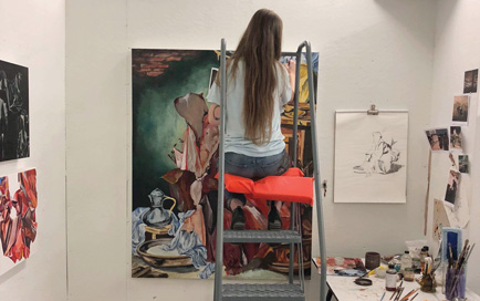 Student painting while sitting on a ladder