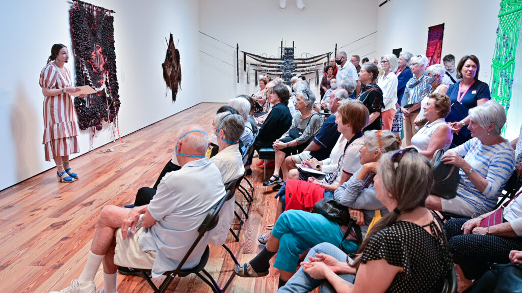 Curator Emilee Enders giving a tour of the exhibition A Beautiful Mess: Weavers & Knotters of the Vanguard on Feb. 25 on view at Sarasota Art Museum through June 25. Works by Jacqueline Surdell, Kira Dominguez Hultgren, dani lopez, and Dana Hemenway hang behind Enders who is curator for the Bedford Gallery at the Lesher Center for the Arts in Walnut Creek, CA.