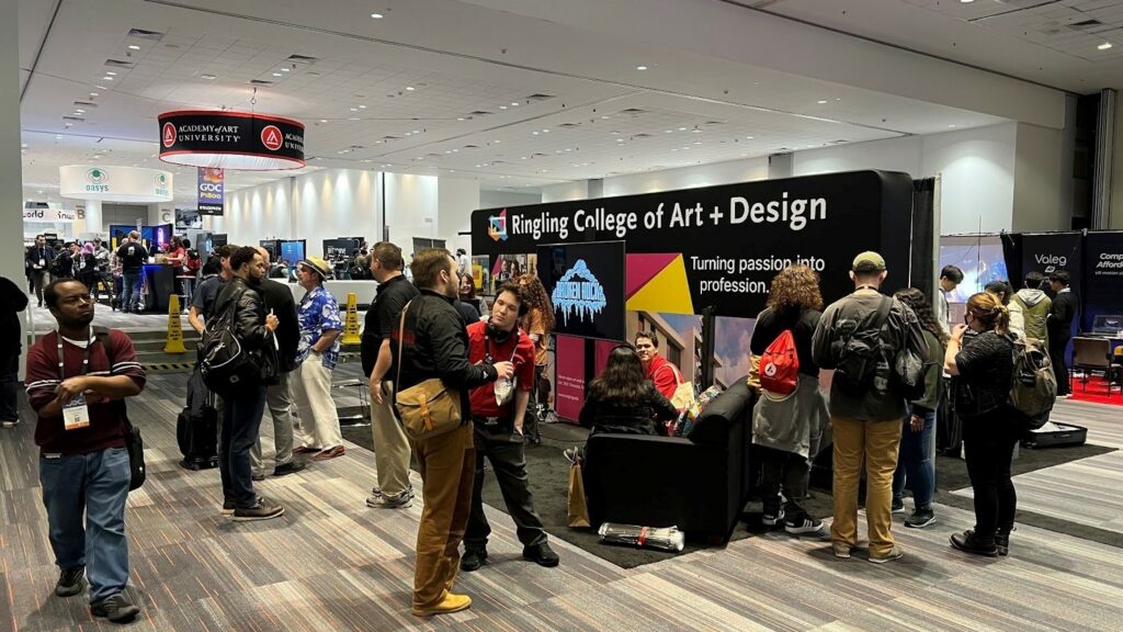 Ringling College’s booth is displayed at a large conference hall with several people in attendance