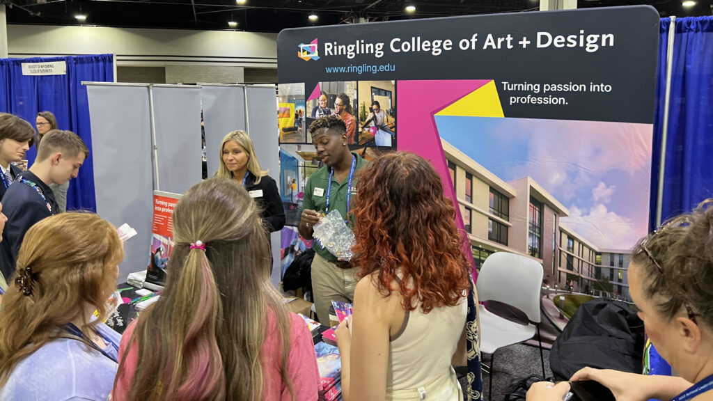 Ringling admissions counselors standing at booth surrounded by a crowd of young adults.