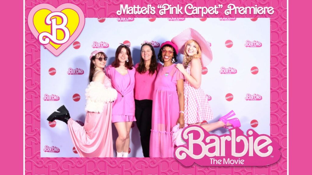 Five women stand in front of Barbie branded background all wearing pink outfits