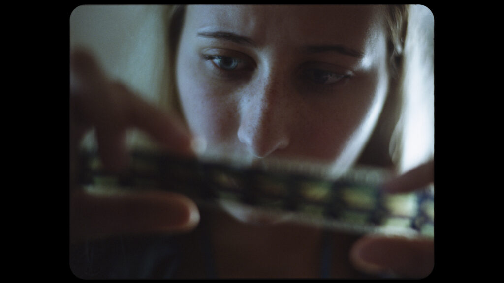 Still frame from a film project of closeup of a blonde girl looking at a roll of film.