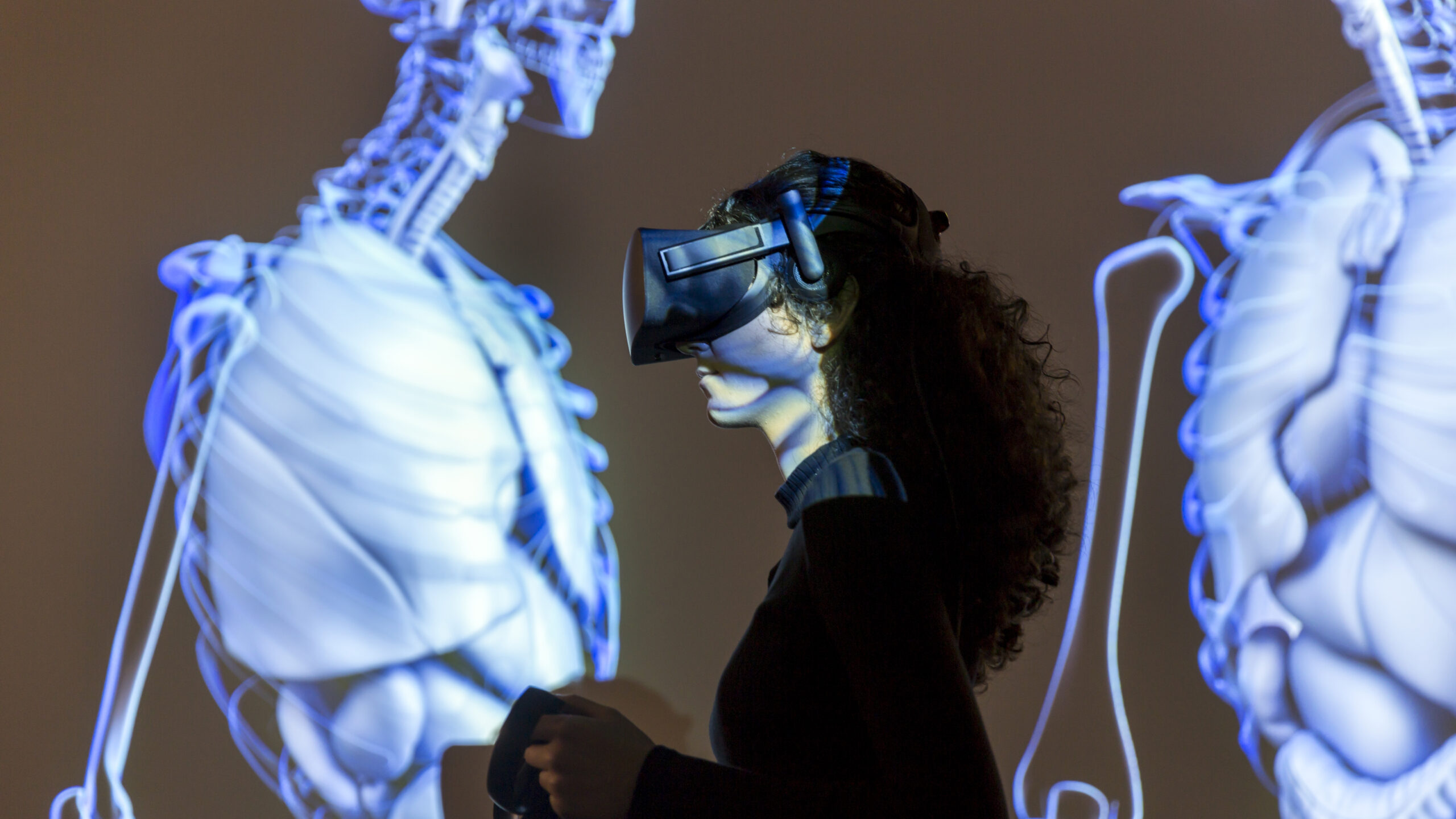 A girl with a VR headset stands in front of a lifesize protected human skeleton