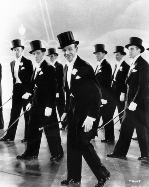 1930s men dressed in tuxedos performing in a choreographed routine