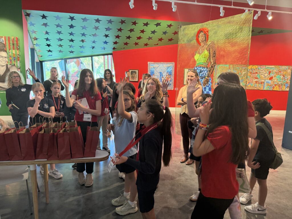 A group of elementary students raising their hands in the gallery. 