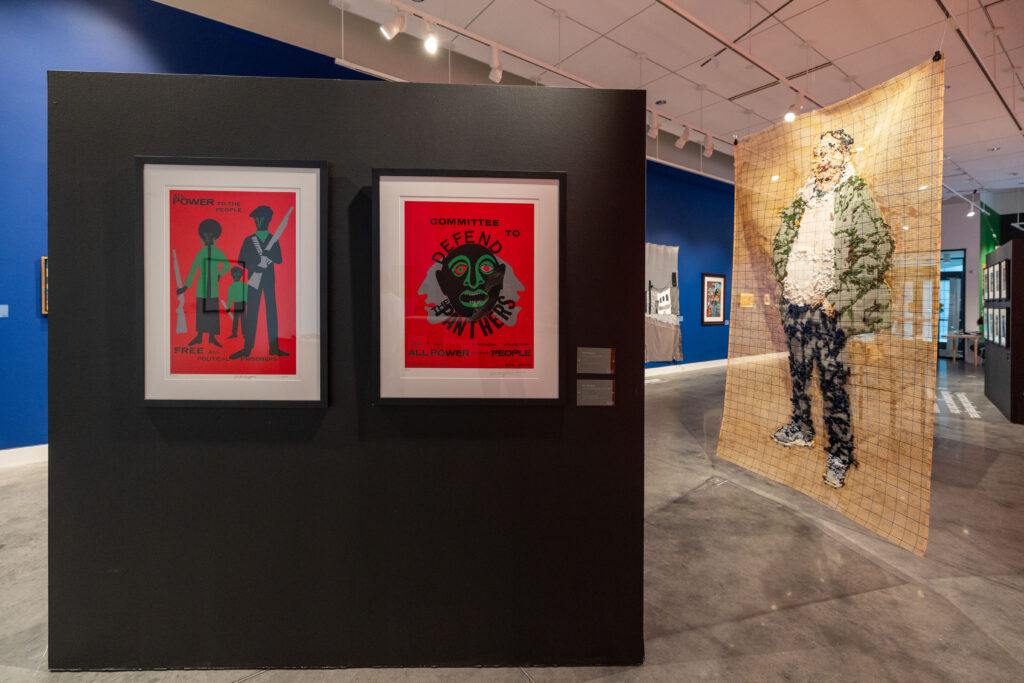 Two print artworks with red backgrounds on a small black wall in the middle of a gallery.  