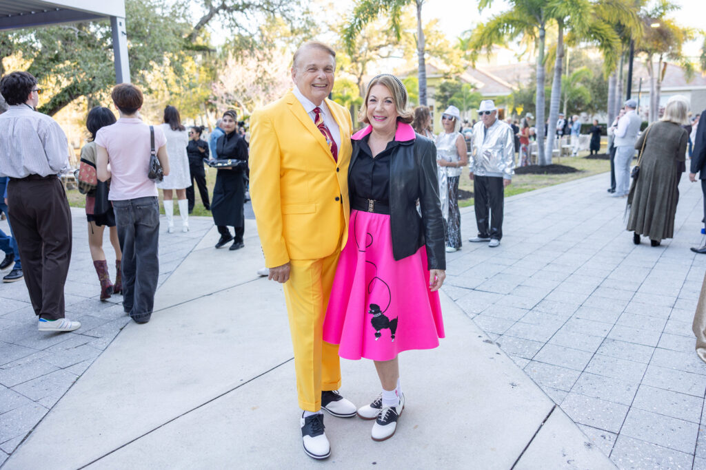 Alumni in Colorful Outfits Two alumni posing outdoors, one wearing a bright yellow suit and the other a pink skirt.