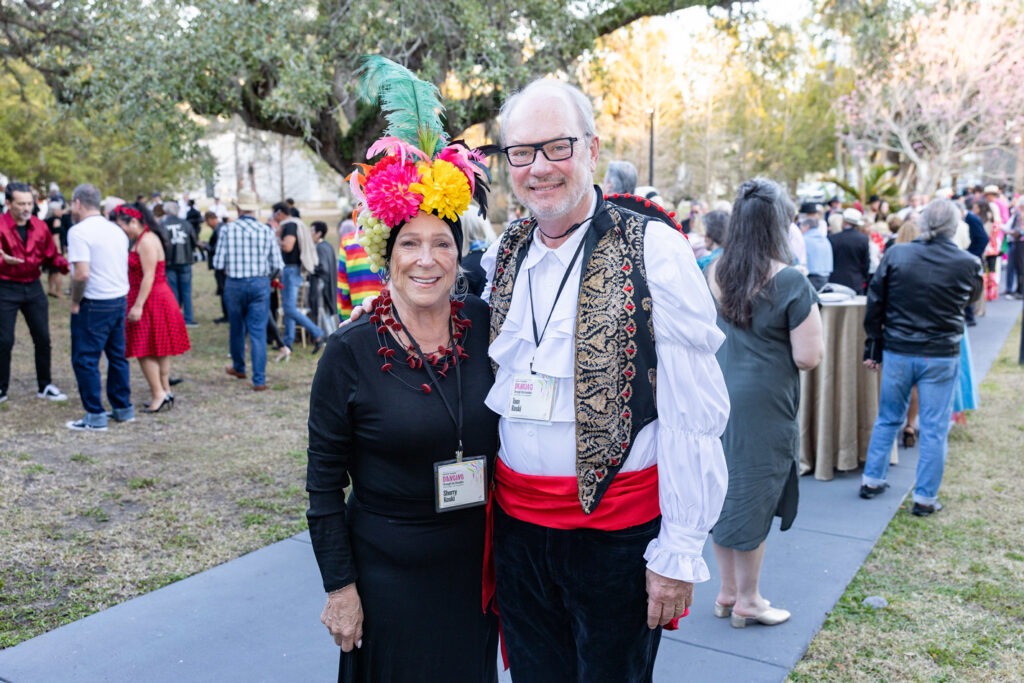 Alumni in Festive Attire Two alumni posing together at an outdoor event, one wearing a colorful headpiece.