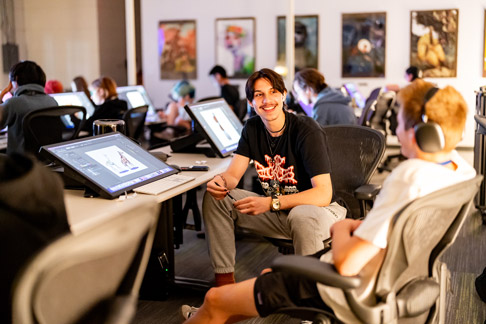 Students sit at computer workstations in a classroom, collaborating and working on digital design projects.