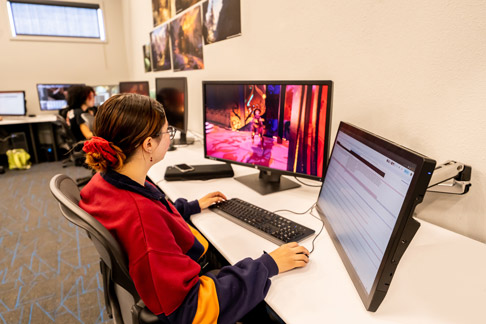 Student using dual monitors at a workstation in a digital media lab, editing content on a computer