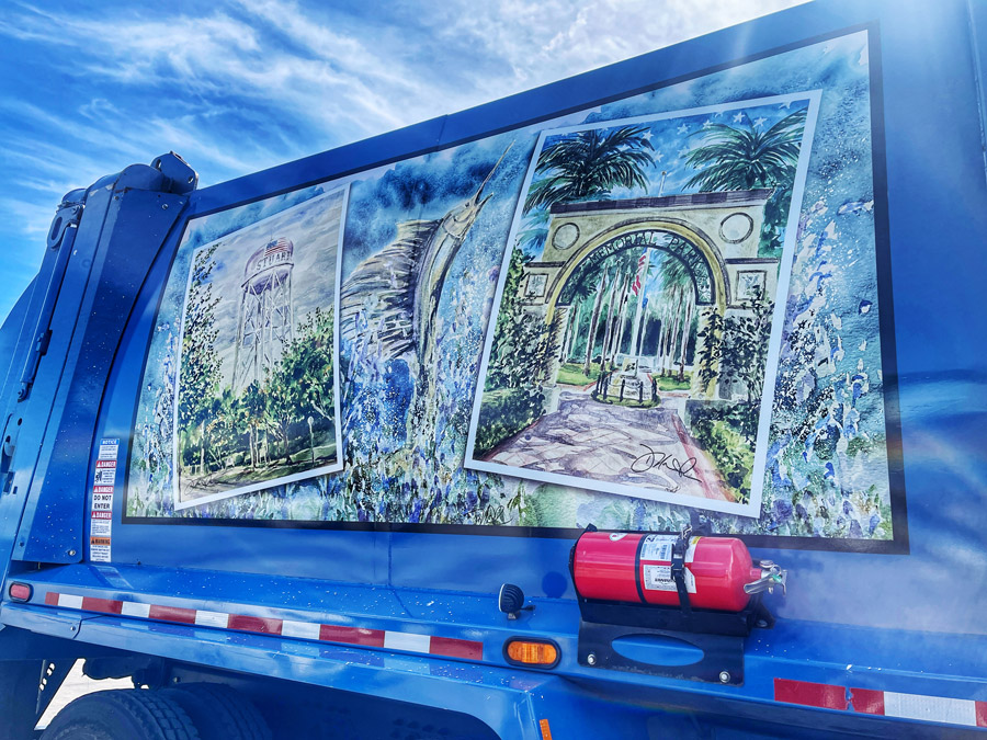 Close-up of a painted collage mural on the side of a blue truck, featuring scenic architectural arches and lush greenery
