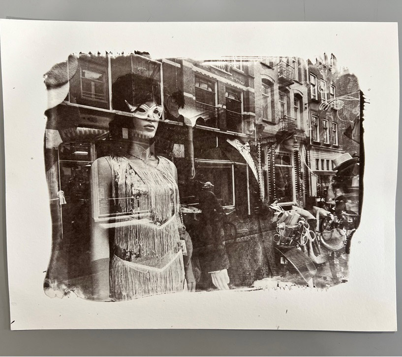 Black-and-white photographic collage showing a layered street scene with a figure reflected in storefront glass