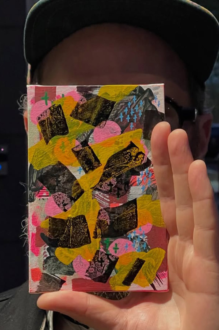 Hand holding a colorful mixed-media artwork featuring layered textures, bold shapes, and abstract patterns in vibrant colors