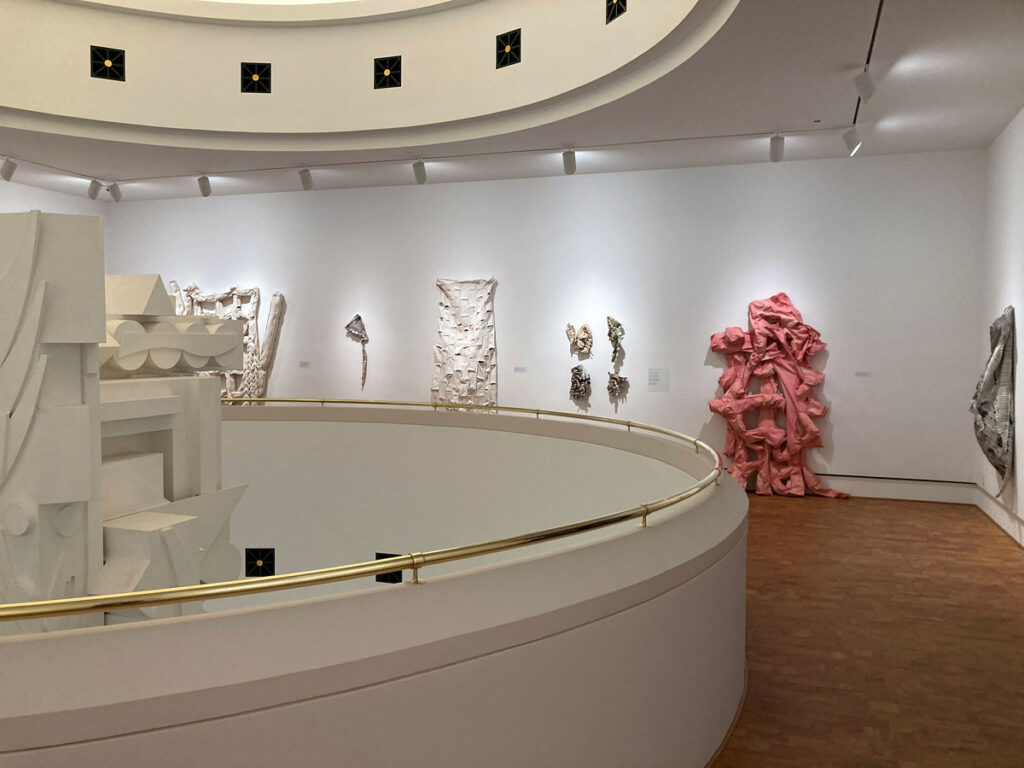 Curved gallery interior featuring abstract sculptural works in white and pink materials along the walls