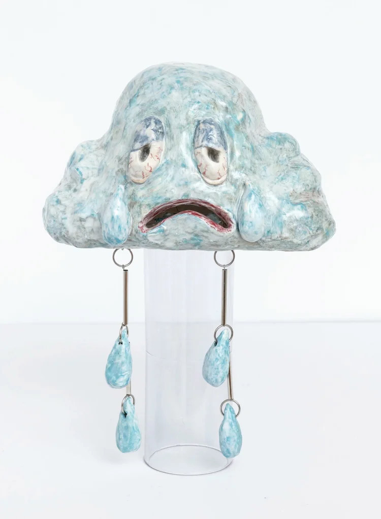 Ceramic cloud sculpture with a sad expression and hanging teardrop forms on a transparent stand