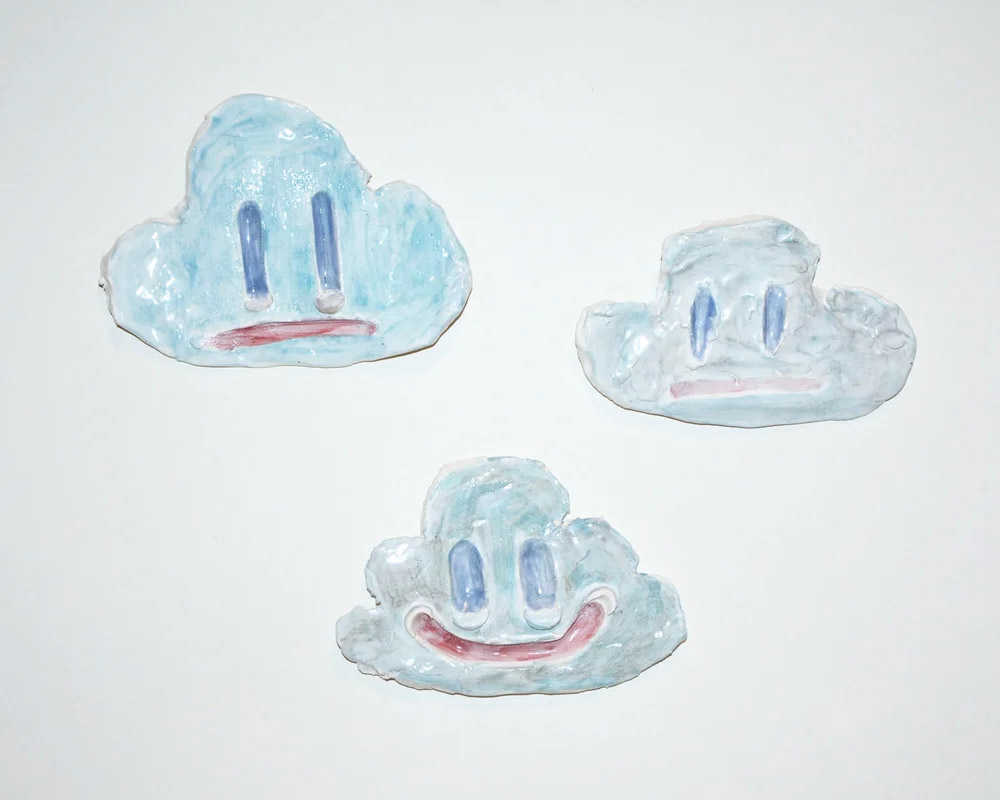 Group of three ceramic cloud faces with varied expressions mounted on a white wall