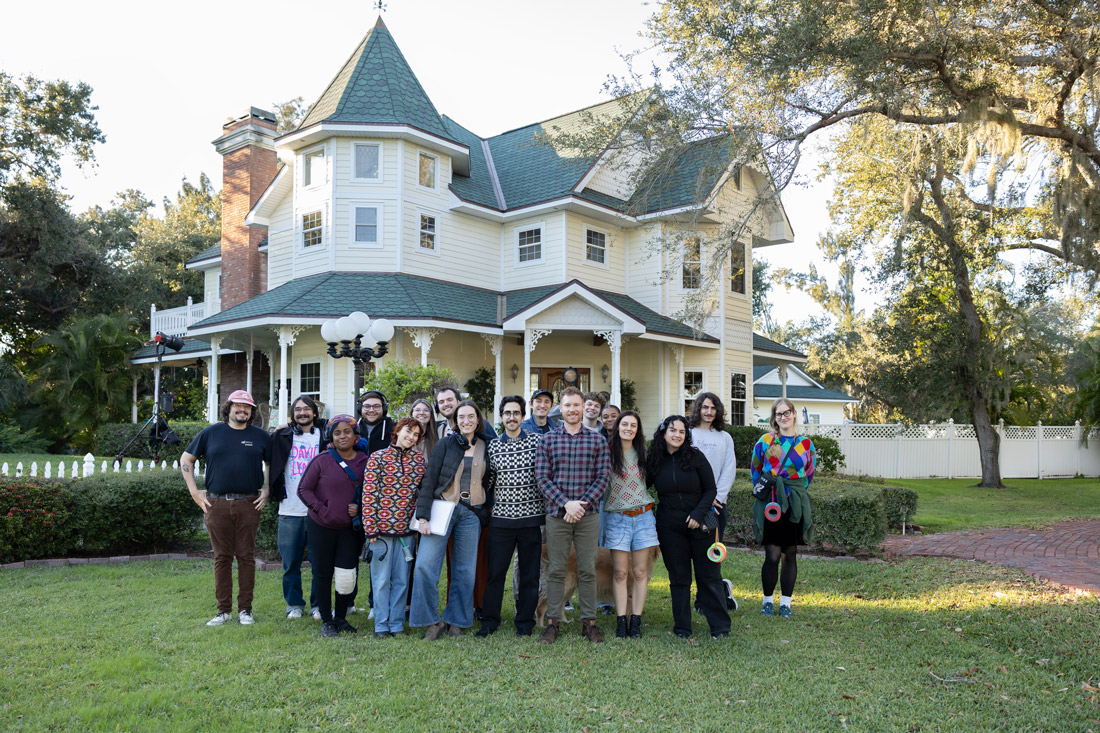 Cast and crew group photo standing on a lawn in front of a large historic house