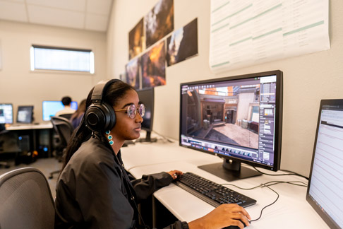 Student wearing headphones working on a computer with a digital design project open on screen in a classroom setting.