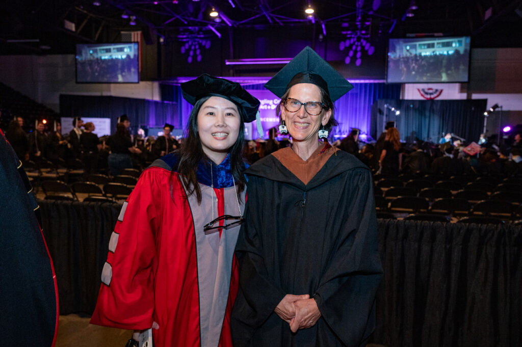 Graduate and Faculty Portrait Graduate smiling beside faculty member during ceremony celebration.