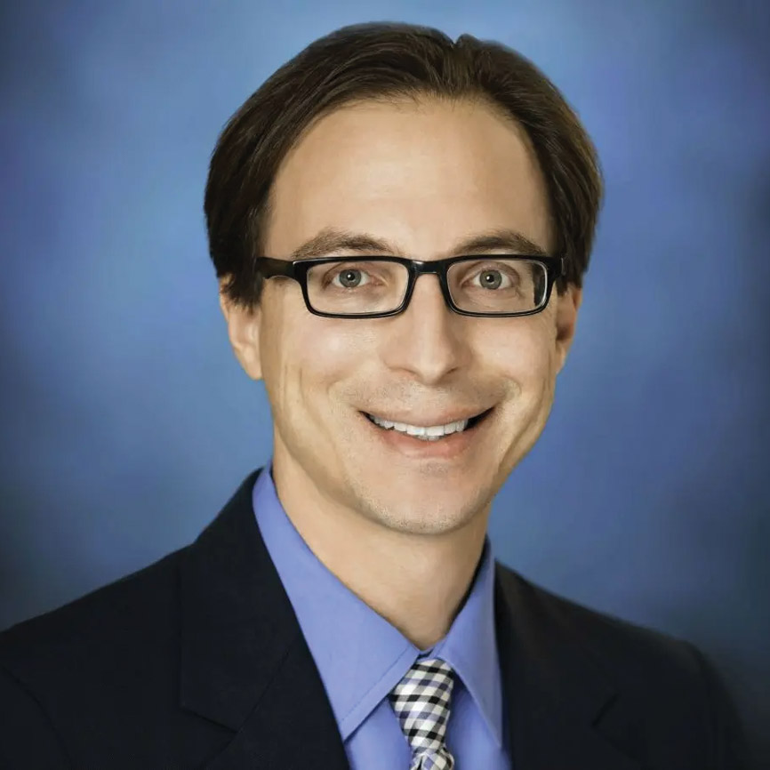Portrait of Dr. Davis Schneiderman smiling outdoors in a blue button-down shirt.