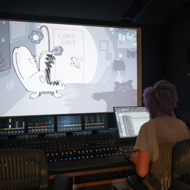 student at sound board looking at black and white animation on large screen