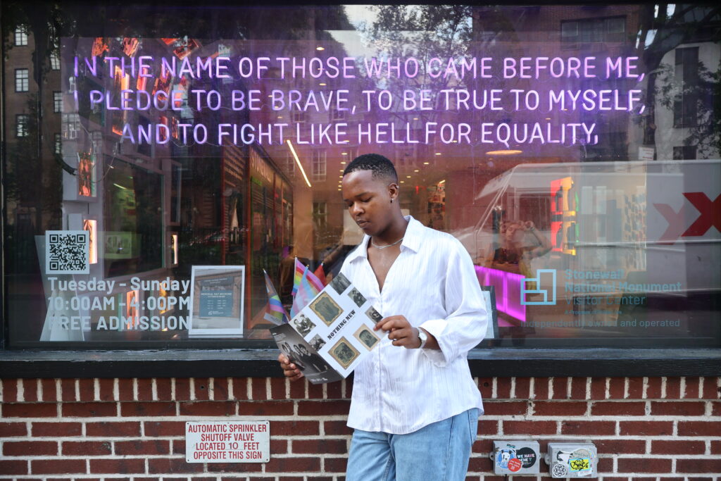 person reading in front of large storefront window with purple neon text above.